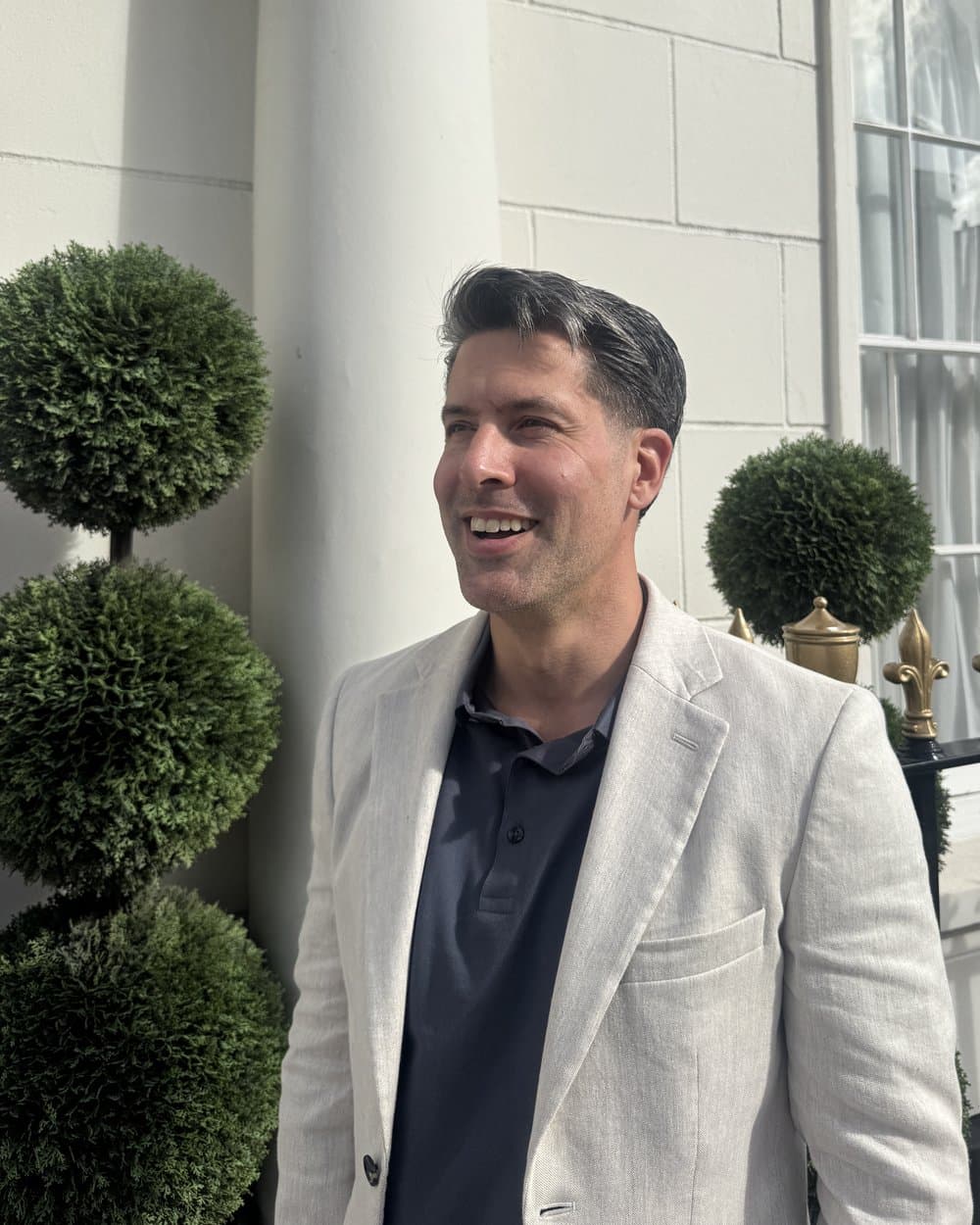 Matt Dagworthy, smiling, in a linen jacket outside a white townhouse